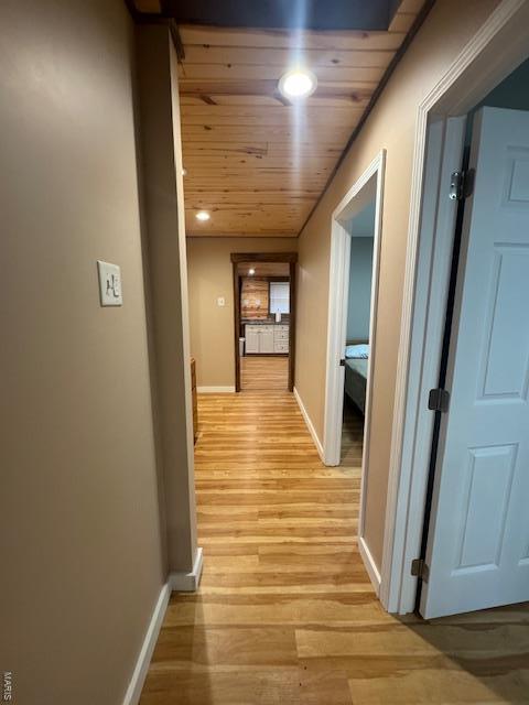 hallway featuring light wood-type flooring, baseboards, and wood ceiling