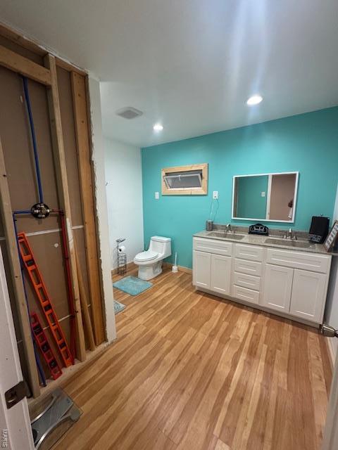 bathroom featuring a sink, toilet, recessed lighting, double vanity, and wood finished floors