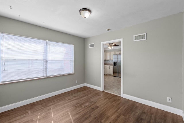 spare room with wood finished floors, ceiling fan, baseboards, and visible vents
