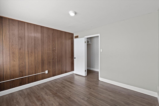 unfurnished room featuring visible vents, baseboards, wood walls, and dark wood finished floors
