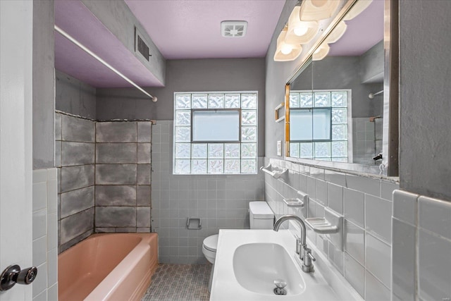 full bathroom with a sink, tile walls, toilet, tile patterned flooring, and bathing tub / shower combination
