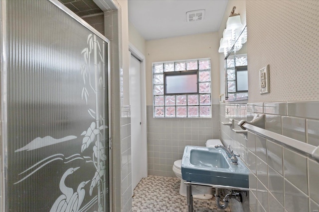 bathroom with a sink, tile walls, toilet, a shower stall, and a wainscoted wall