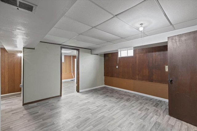 basement with light wood-type flooring, a paneled ceiling, baseboards, and visible vents