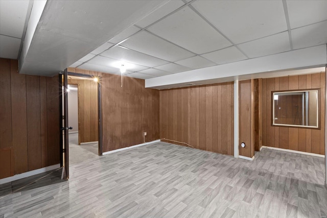 finished below grade area featuring wood walls, baseboards, a drop ceiling, and light wood-style floors