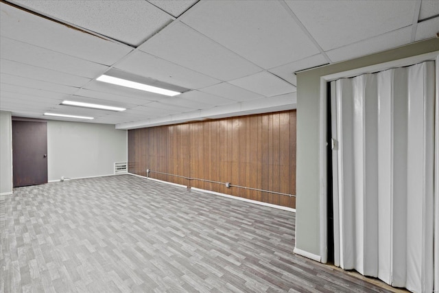 finished below grade area featuring wood walls, baseboards, a paneled ceiling, and wood finished floors