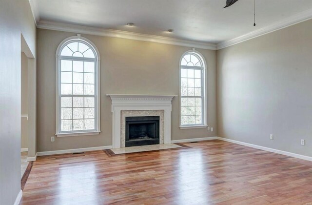unfurnished living room featuring a premium fireplace, wood finished floors, baseboards, and ornamental molding