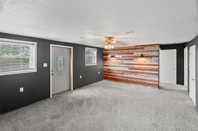 carpeted entrance foyer with wooden walls, a textured ceiling, visible vents, and a ceiling fan