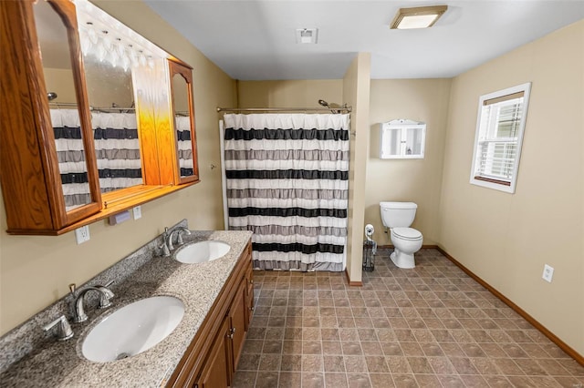 bathroom with baseboards, toilet, double vanity, and a sink