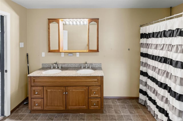 full bathroom with baseboards, stone finish floor, double vanity, and a sink
