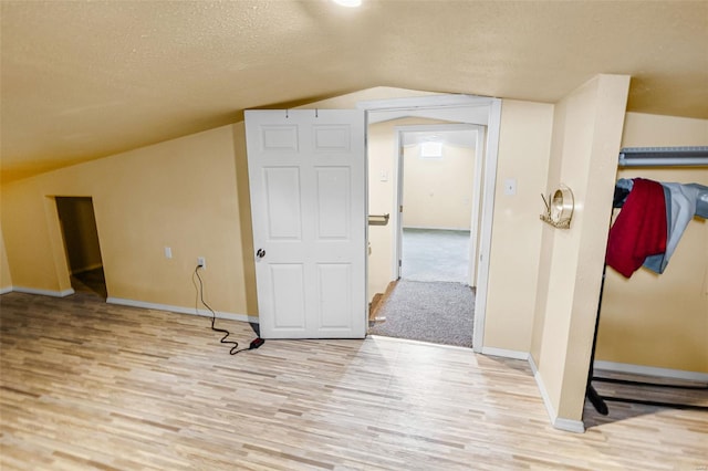 additional living space with a textured ceiling, baseboards, lofted ceiling, and light wood-style floors
