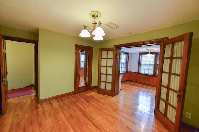 empty room with french doors, baseboards, light wood finished floors, and a chandelier