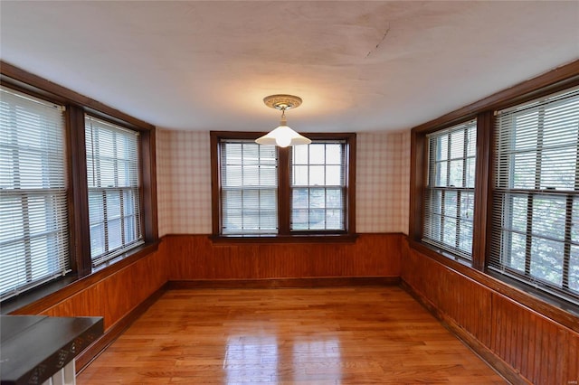 unfurnished dining area with a wainscoted wall, light wood-style floors, and wallpapered walls