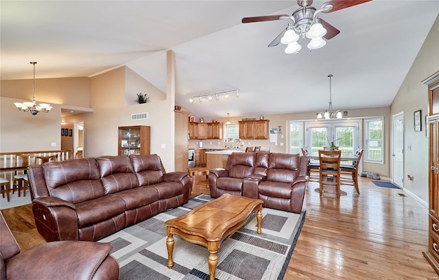 living area with rail lighting, light wood-type flooring, ceiling fan with notable chandelier, visible vents, and lofted ceiling