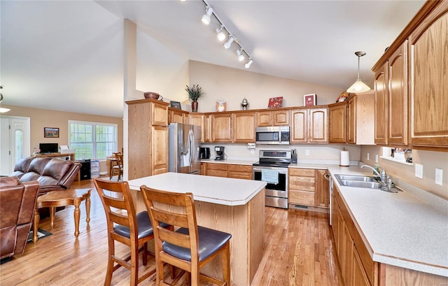 kitchen with a sink, appliances with stainless steel finishes, a breakfast bar, open floor plan, and track lighting