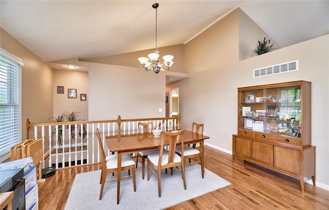 dining area featuring an inviting chandelier, high vaulted ceiling, light wood-type flooring, visible vents, and baseboards