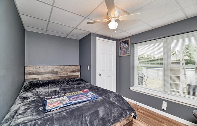 bedroom with ceiling fan, a drop ceiling, wood finished floors, and baseboards