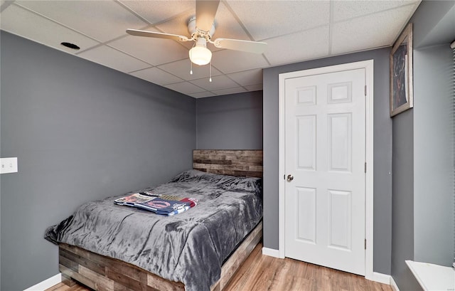 bedroom with baseboards, wood finished floors, a ceiling fan, and a drop ceiling