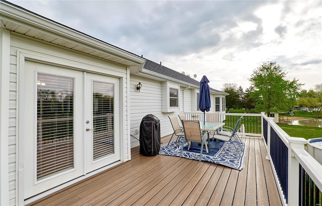 wooden deck with outdoor dining space, a water view, and french doors