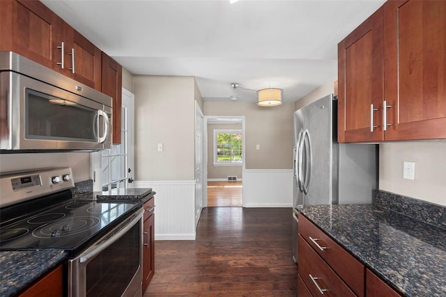 kitchen with dark wood finished floors, visible vents, dark stone counters, wainscoting, and appliances with stainless steel finishes
