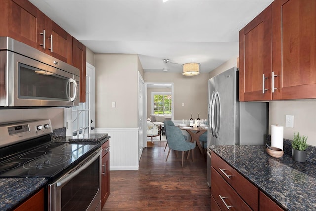 kitchen with dark stone counters, dark wood-style flooring, appliances with stainless steel finishes, and a wainscoted wall