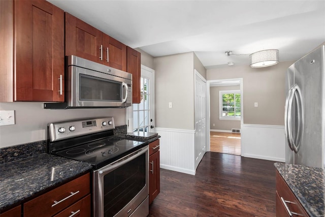 kitchen featuring dark stone countertops, appliances with stainless steel finishes, a wainscoted wall, and dark wood-type flooring
