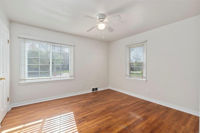 unfurnished room featuring a wealth of natural light, a ceiling fan, wood finished floors, and baseboards