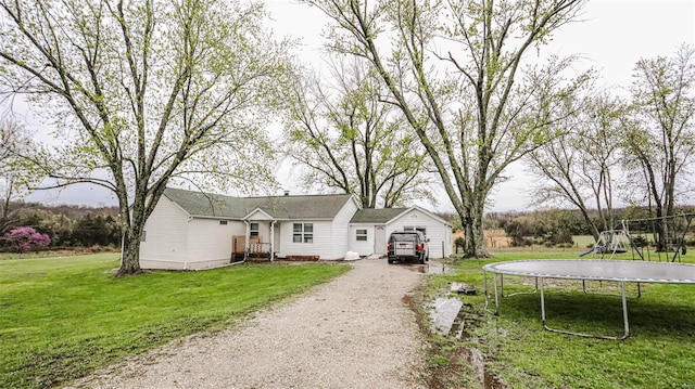 view of front of home with dirt driveway, a front lawn, a trampoline, and a garage