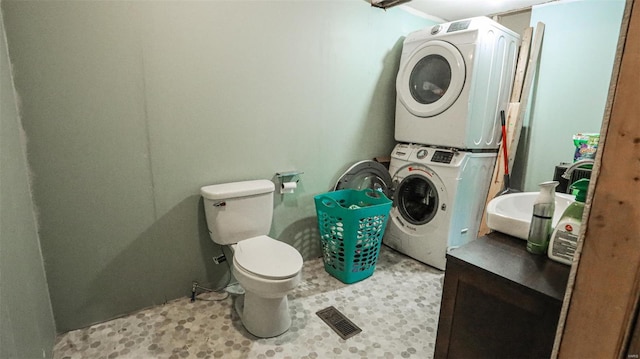 bathroom featuring stacked washer / dryer, visible vents, and toilet