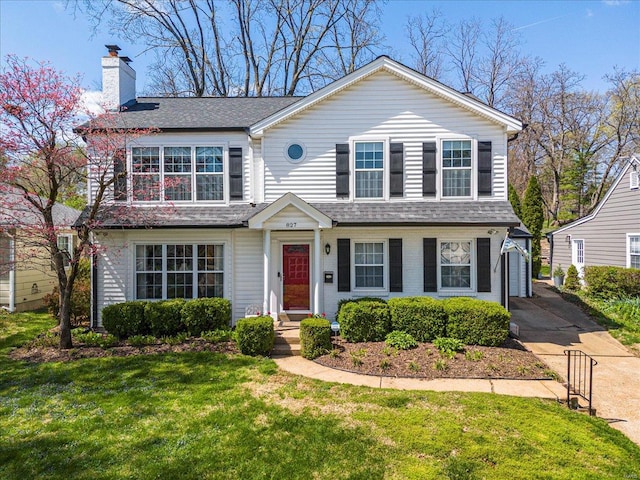 traditional-style home featuring a front yard, a chimney, and roof with shingles