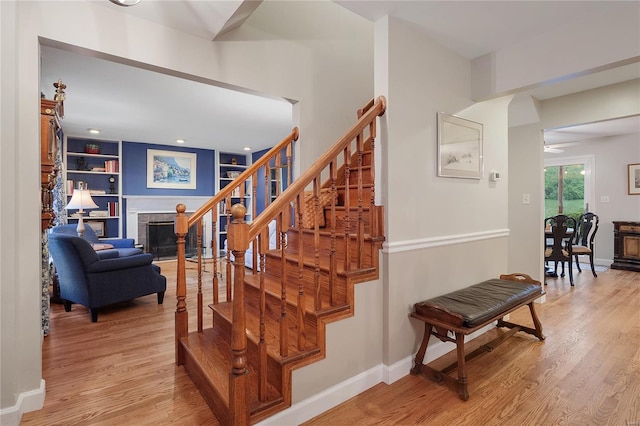 staircase featuring baseboards, wood finished floors, and a brick fireplace