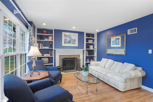 living area with visible vents, built in features, baseboards, a tiled fireplace, and wood finished floors