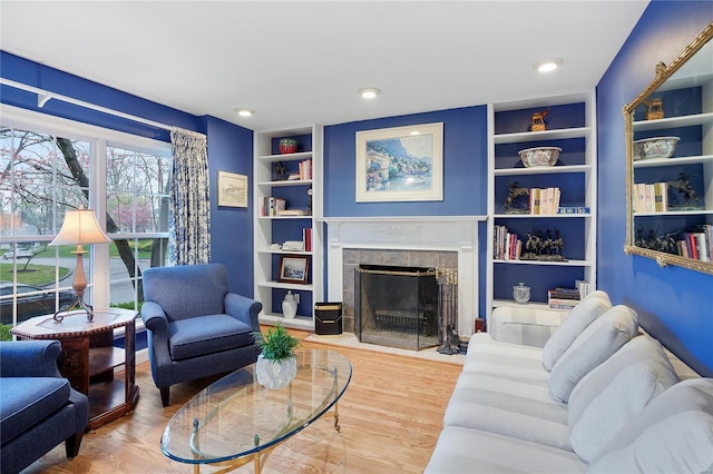 living room with built in features, recessed lighting, a tile fireplace, and wood finished floors