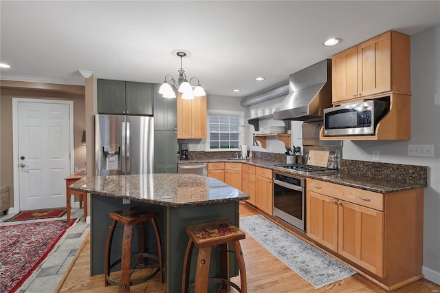 kitchen with dark stone countertops, wall chimney exhaust hood, a sink, stainless steel appliances, and a breakfast bar area
