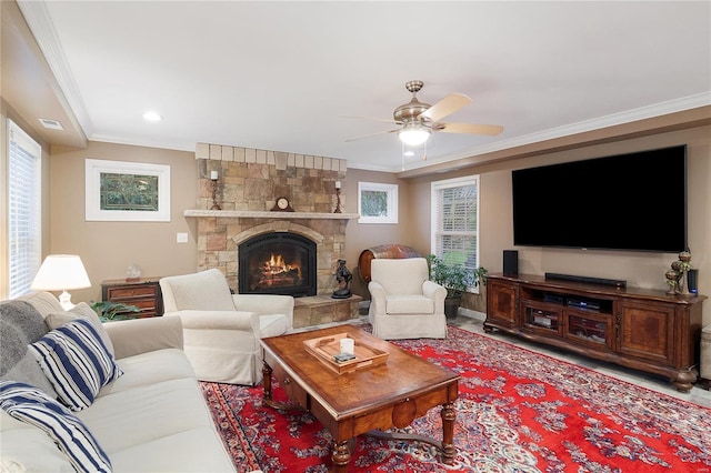 living room featuring a healthy amount of sunlight, ceiling fan, ornamental molding, and a stone fireplace