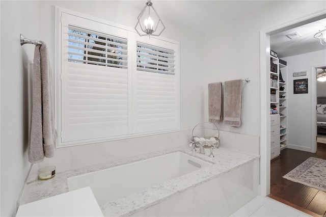 full bathroom with visible vents, a bath, a notable chandelier, a walk in closet, and wood finished floors
