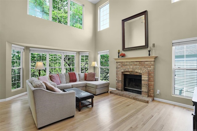living area with baseboards, a high ceiling, a brick fireplace, and wood finished floors