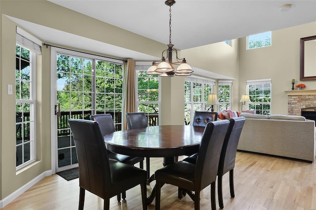 dining space featuring light wood-type flooring, baseboards, a brick fireplace, and an inviting chandelier