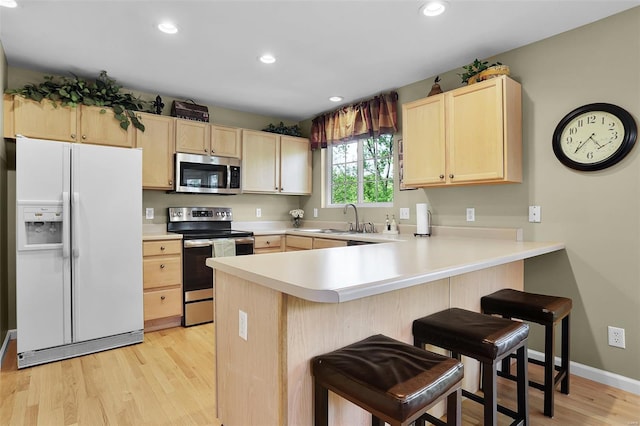 kitchen with a peninsula, light brown cabinetry, light wood-style floors, a sink, and stainless steel appliances