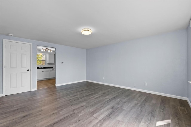 empty room featuring dark wood-style flooring, baseboards, and a sink
