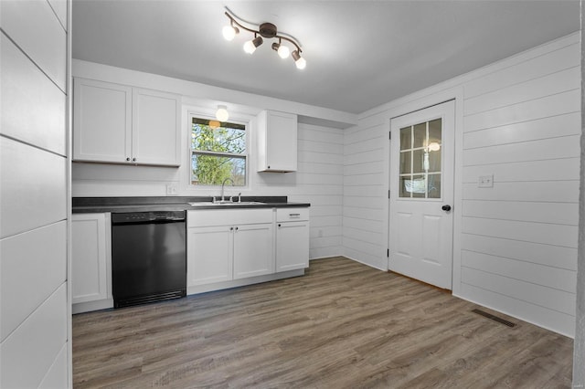 kitchen featuring wood finished floors, dishwasher, a sink, and dark countertops