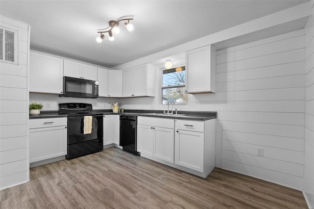 kitchen with light wood-style flooring, dark countertops, white cabinetry, and black appliances