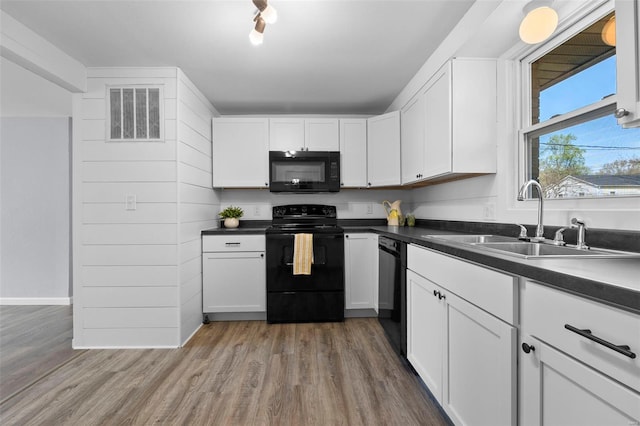 kitchen featuring white cabinetry, black appliances, wood finished floors, a sink, and dark countertops