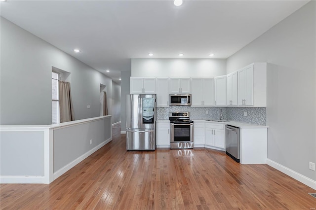 kitchen featuring light countertops, tasteful backsplash, a sink, light wood-style flooring, and appliances with stainless steel finishes