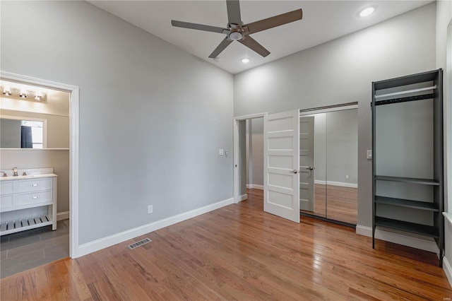 unfurnished bedroom with a sink, light wood-style floors, high vaulted ceiling, baseboards, and visible vents