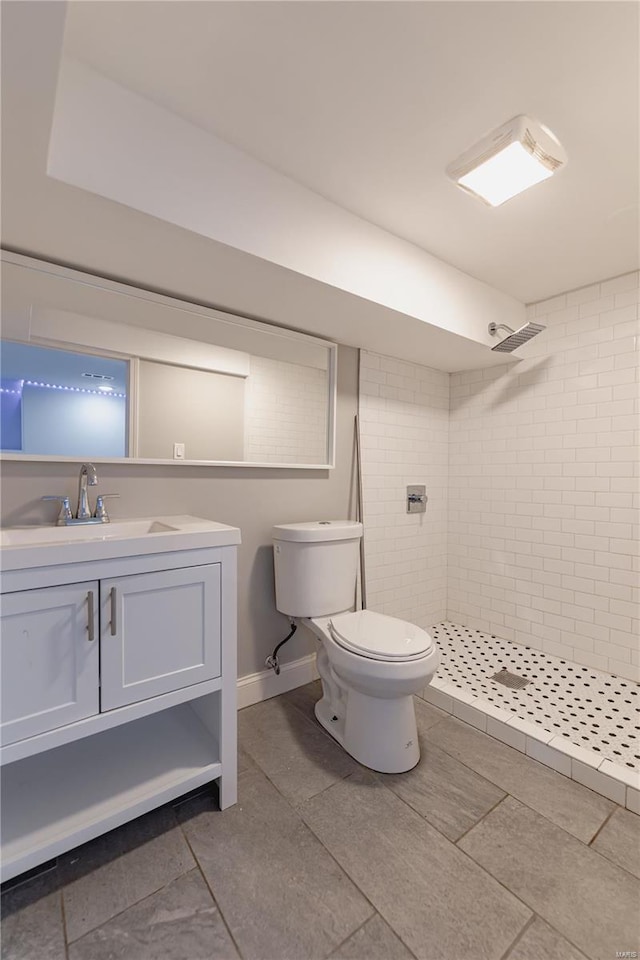 full bathroom with vanity, baseboards, a tile shower, and toilet