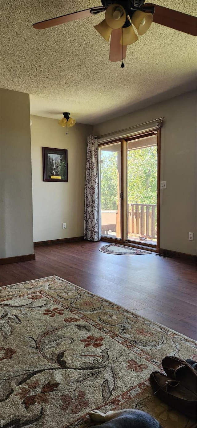 empty room with a textured ceiling, wood finished floors, ceiling fan, and baseboards