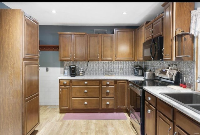 kitchen with stainless steel range with electric cooktop, black microwave, brown cabinetry, light countertops, and light wood finished floors