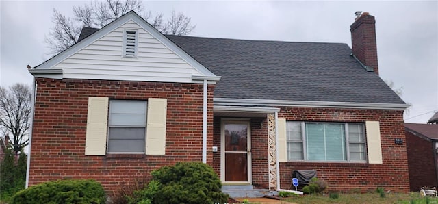 view of front of property with a chimney, a shingled roof, and brick siding