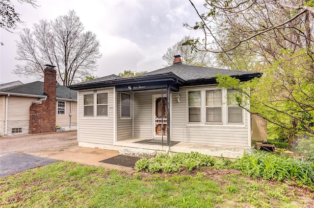 bungalow-style house featuring a porch, a shingled roof, and a chimney