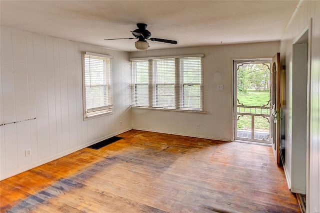 empty room featuring a ceiling fan, wood finished floors, and a healthy amount of sunlight